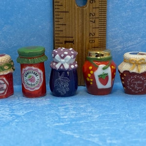 May include: Five miniature ceramic jars with lids, each decorated with a different fruit design and label. The jars are labeled "Confiture de Groseilles", "Confiture de Framboises", "Confiture de Figues", "Confiture de Cassis", and "Confiture de Fraises".
