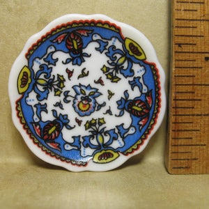 May include: A small, white ceramic plate with a blue and white floral design. The plate has a scalloped edge and is decorated with red, yellow, and blue flowers.