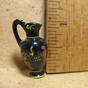 May include: A small black ceramic pitcher with a yellow and red floral design. The pitcher is about 2 inches tall.