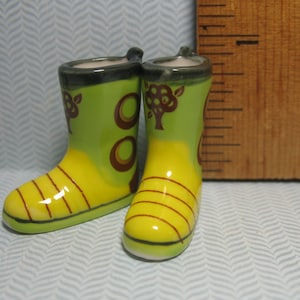 May include: A pair of yellow and green ceramic rain boots with a brown tree design. The boots are about 3 inches tall.