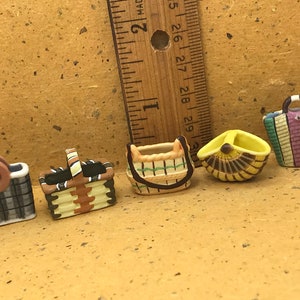 May include: Five miniature ceramic baskets with different patterns and colours. The baskets are arranged in a row on a brown surface. The baskets are approximately 2.5 cm tall.