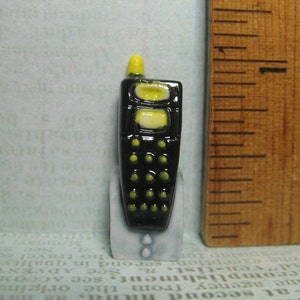 Puede incluir: Una pequeña figurita de cerámica negra y amarilla de un teléfono móvil vintage con una antena amarilla.