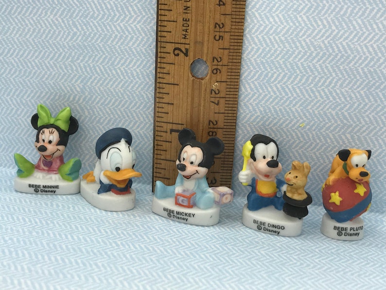 Może przedstawiać: Zestaw pięciu porcelanowych figurek postaci z Disneya, w tym Myszki Miki, Minnie Mouse, Kaczora Donalda, Goofy'ego i Pluto. Każda figurka ma około 5 cm wysokości i przedstawia postać w dziecięcej pozie. Figurki są pomalowane żywymi kolorami i mają błyszczące wykończenie.