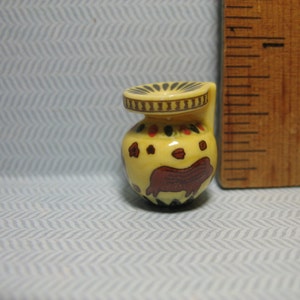 May include: A small, yellow ceramic vase with a brown and red design. The vase has a wide mouth and a narrow neck.