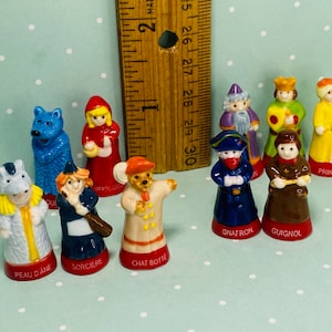 Könnte beinhalten: Ein Set aus zehn Porzellanfiguren, die Figuren aus klassischen Märchen darstellen. Die Figuren sind in leuchtenden Farben bemalt und zeigen Details wie einen Wolf, ein Rotkäppchen, eine Katze, eine Prinzessin und einen Zauberer. Jede Figur hat einen Namen auf dem Sockel.