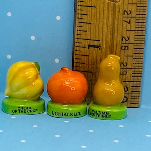 May include: Three miniature ceramic squash figurines, each with a different variety name. The first is labeled "Cream of the Crop", the second is labeled "Uchiki Kuri", and the third is labeled "Waltham Butternut".