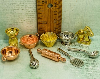 May include: A set of miniature kitchen tools and appliances, including a copper mixing bowl, a rolling pin, a whisk, a spatula, a colander, a cupcake liner, a scale, and a stand mixer. The tools are made of metal and have a shiny finish.
