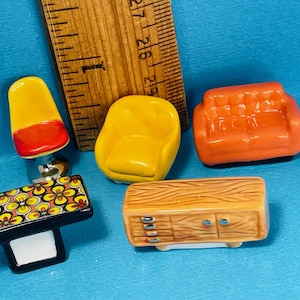 Puede incluir: Conjunto de muebles en miniatura que incluye una silla amarilla, un sofá naranja y un mueble con aspecto de madera. También se incluye una mesa en blanco y negro con diseño floral y una silla amarilla y roja. Una regla de madera está presente.