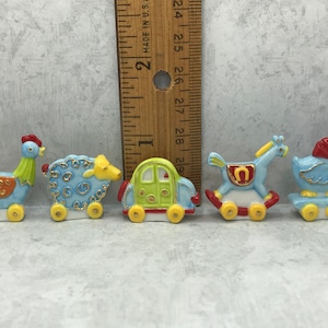 Puede incluir: Cinco figuritas de cerámica en miniatura de animales de granja y un coche. Las figuritas están pintadas en colores brillantes, incluyendo azul, verde, amarillo, rojo y naranja. Las figuritas están sobre un fondo gris.