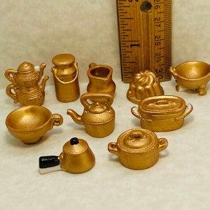 Puede incluir: Un conjunto de diez artículos de cocina en miniatura de color dorado, que incluyen una tetera, una jarra de leche, una tetera, una fuente para hornear, un tazón y un molde para hornear.