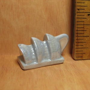 Könnte beinhalten: Eine kleine, weiße Keramikfigur des Opernhauses von Sydney. Die Figur ist mit einer strukturierten Oberfläche detailliert und etwa 5 cm hoch.