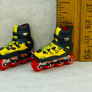 Könnte beinhalten: Ein Paar Miniatur-Rollschuhe in Gelb und Schwarz mit roten Rollen. Die Rollschuhe sind etwa 5 cm hoch.