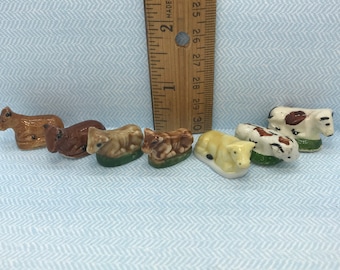May include: A set of six miniature ceramic cows in various brown, white, and black patterns. The cows are lying down and are about 1 inch long.