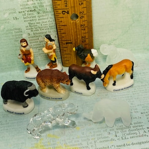 May include: A collection of miniature figurines depicting various animals, including a bear, a bull, a horse, a boar, a turkey, and a human. The figurines are made of porcelain and are painted in realistic colors. The figurines are displayed on a white surface with a ruler for scale.