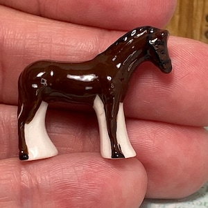May include: A miniature ceramic horse figurine. The horse is brown with white legs and a white blaze on its face. The figurine is glossy and detailed, showcasing the horse's form.
