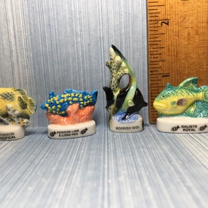 May include: Four miniature ceramic figurines of colorful fish. The fish are on small bases with French names. The names are "Poisson Tropical", "Poisson Lime a Long Nez", "Moorish Idol", and "Baliste Royal".