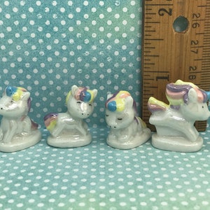 May include: Four small ceramic unicorn figurines with rainbow manes and tails. The unicorns are in various poses, including standing, sitting, and lying down. The figurines are about 1 inch tall.