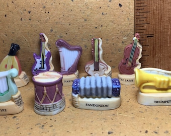 May include: A collection of miniature musical instruments, including a lyre, harp, guitar, drum, accordion, bass, and trumpet. Each instrument is painted in bright colors and has a detailed design.
