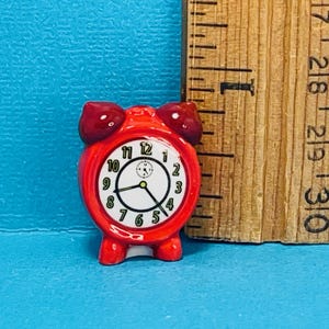 May include: A red ceramic alarm clock with white face and black numbers. The clock has a small second hand in the center. The clock is about 2 inches tall.
