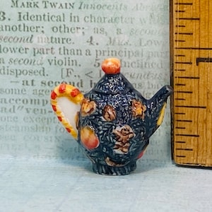 May include: A small blue teapot with a yellow and red handle and a floral design. The teapot is approximately 5 cm tall and is made of ceramic.
