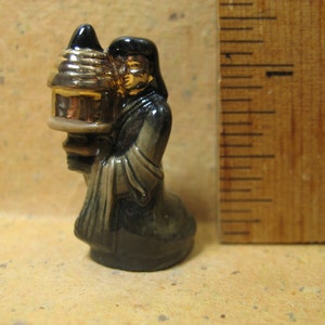 May include: A small ceramic figurine of a person wearing a black robe and holding a gold and brown lantern.
