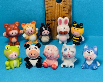 May include: A collection of ten small, colorful animal figurines. The figurines include a bear, tiger, panda, pig, cat, wolf, frog, bee, bunny, and a bat. The figurines are made of ceramic and are painted with bright colors. A wooden ruler is in the background.