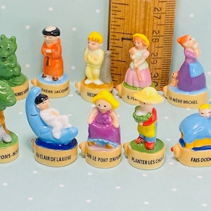 Könnte beinhalten: Ein Set mit zehn Miniatur-Porzellanfiguren, die Szenen aus dem französischen Kinderbuch "Die kleine Raupe Nimmersatt" von Eric Carle darstellen. Die Figuren sind in leuchtenden Farben bemalt und zeigen Figuren wie die Raupe, den Schmetterling und den Apfel.
