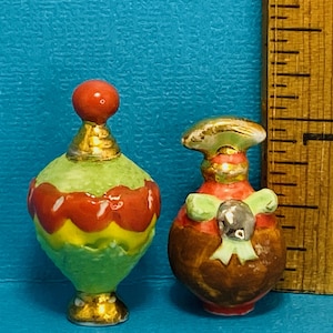 Puede incluir: Dos botellas de perfume en miniatura de cerámica con diseños intrincados. Una botella es verde con acentos rojos y amarillos, la otra es marrón con acentos verdes y dorados.