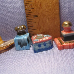 May include: Four miniature ceramic figurines, including a blue and gold bottle, a pink and gold candlestick, a blue and white heart-shaped dish, and a brown and gold boat-shaped dish.