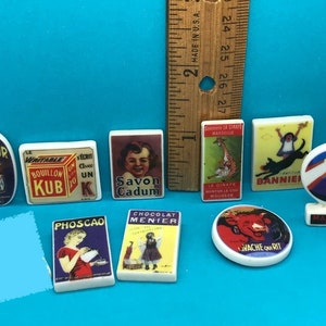 Może przedstawiać: Kolekcja vintage francuskich płytek reklamowych przedstawiających różne produkty, w tym mydło, bulion, czekoladę i żyrafę. Płytki są białe z kolorowymi obrazami i tekstem.