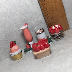Puede incluir: Un conjunto de figuritas de cerámica en miniatura con temática de fresa, que incluye un batido de fresa, un cucurucho de helado de fresa, una cesta de fresas y un postre de fresa.