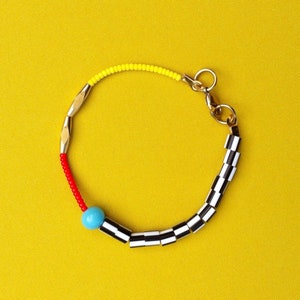 May include: A colourful beaded bracelet with a black and white chequered pattern, a red section, a yellow section, and a turquoise bead.