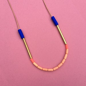 May include: A gold necklace featuring blue and peach coloured beads. The necklace is made from a thin gold chain with a series of small, rectangular beads in peach and two larger, cylindrical beads in blue.