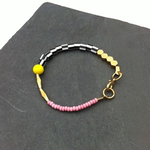 Peut inclure: Un bracelet en or avec des perles noires et blanches en damier, une perle jaune et des perles roses. Le bracelet a un fermoir en or.