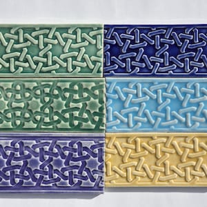 Könnte beinhalten: Sechs rechteckige Keramikfliesen mit einem sich wiederholenden, ineinandergreifenden Muster. Die Fliesen sind in zwei Reihen zu je drei Stück angeordnet und zeigen eine Vielzahl von Farben, darunter Grün, Blau und Gelb. Die Fliesen sind wahrscheinlich für dekorative Zwecke bestimmt.