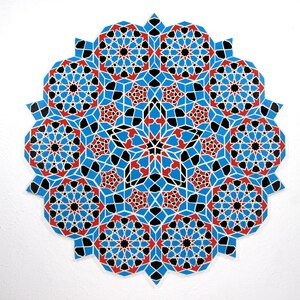 May include: A circular, geometric design featuring a complex pattern of interlocking shapes. The design is primarily blue, with red and black accents, creating a visually striking and symmetrical artwork. The piece is set against a white background.