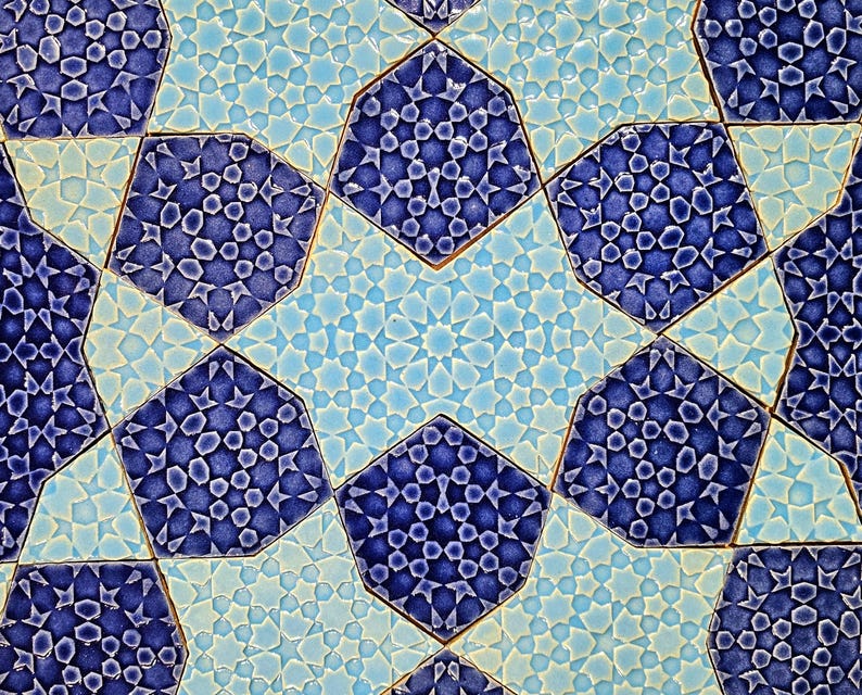 May include: Close-up of a geometric tile pattern in shades of blue and light blue. The design features octagonal shapes with intricate star and dot patterns, creating a mosaic effect. The tiles have a textured, glazed appearance.