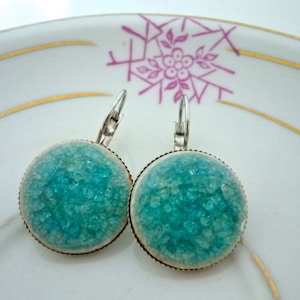 May include: A pair of silver dangle earrings with turquoise blue round glass cabochons. The glass has a textured, sparkly finish.