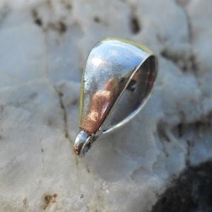 May include: Silver-toned metal pendant bail with a smooth, rounded shape. The bail has a loop at the top for attaching a chain or cord.