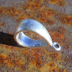 May include: A polished silver pendant in a teardrop shape with a small loop for a chain. The pendant has a smooth, curved surface and a hollow interior. The metal is stamped with "925" and "C26".