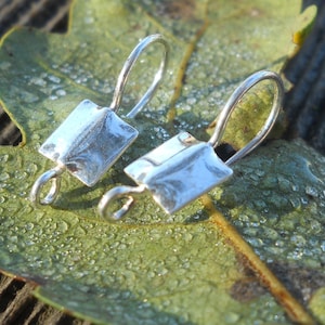 May include: Two silver earring hooks with a square-shaped design. The hooks are made of metal and have a shiny finish.