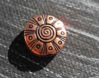 May include: A copper-colored round bead with a black spiral design and a black outline. The bead has a textured surface.
