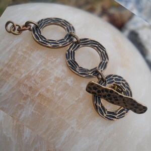 May include: A bronze bracelet with three textured, circular links and a textured, flat bar clasp.