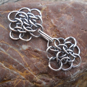 May include: Silver metal clasp with a decorative knot design. The clasp is made of interlocking circles and has a polished finish.