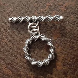 May include: Silver toggle clasp with a twisted rope design and a round ring. The clasp is made of metal and has a polished finish.