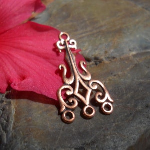 May include: A copper-colored metal pendant with an intricate design featuring a central diamond shape and swirling patterns. The pendant has three open circles at the bottom for attaching to a chain or cord.