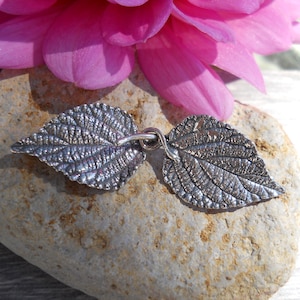 May include: Two silver leaf charms with detailed textured surfaces, connected by a small silver loop.