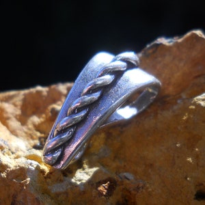 Può includere: Ciondolo in argento con un design a corda intrecciata. Il ciondolo ha la forma di un triangolo curvo.