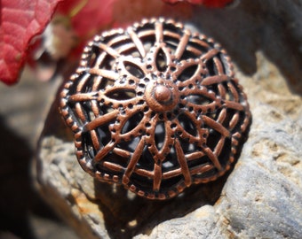 May include: A copper-colored metal charm with a delicate, intricate design. The charm features a circular shape with a central flower-like pattern surrounded by a web-like design.