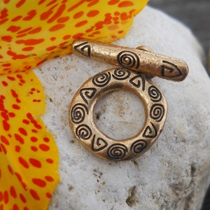 May include: A gold-toned metal ring with a decorative design of spirals and triangles. The ring is on a white surface.